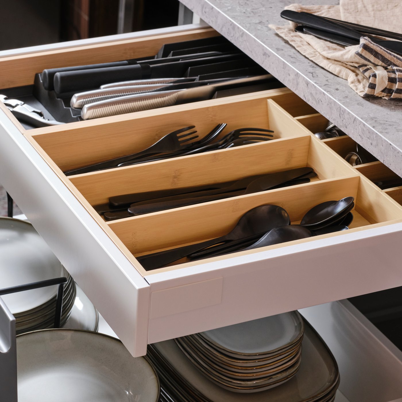 En öppen kökslåda med tallrikar och en annan kökslåda inuti med bestick/knivstället UPPDATERA i ljus bambu.