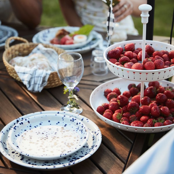 An outdoor table set with glasses, plates, and GARNERA serving plate full of strawberries on Midsummer Eve.