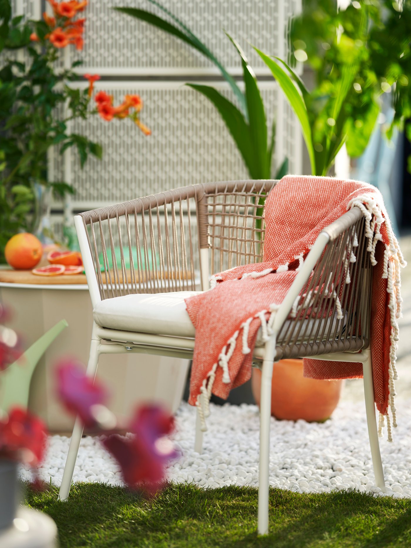 Una silla SEGERÖN con reposabrazos y una manta marrón rojiza colocada encima en un entorno exterior.