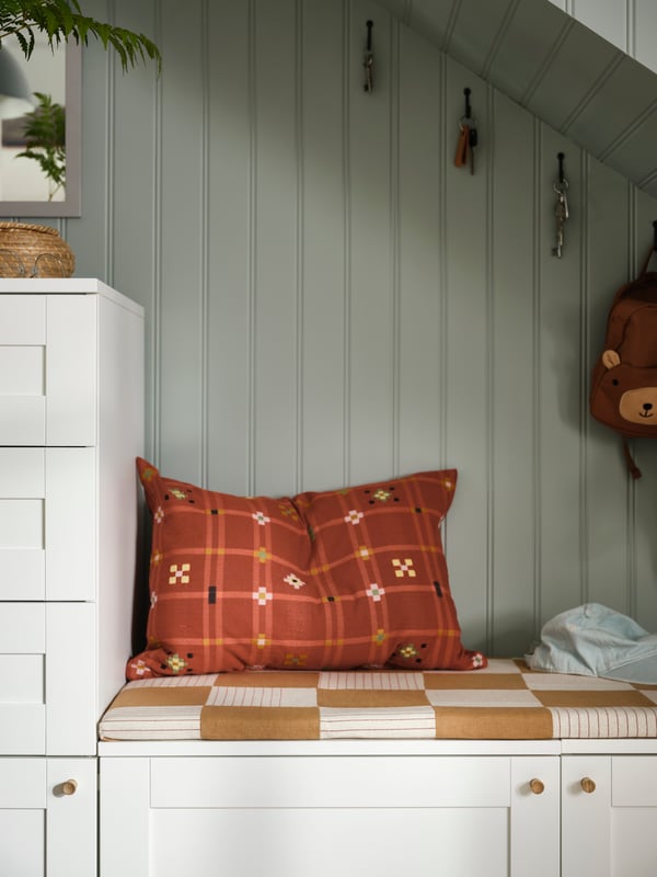 On top of a PLATSA low cupboard is a mattress and a red cushion. The wood panelled wall behind is painted muted green.