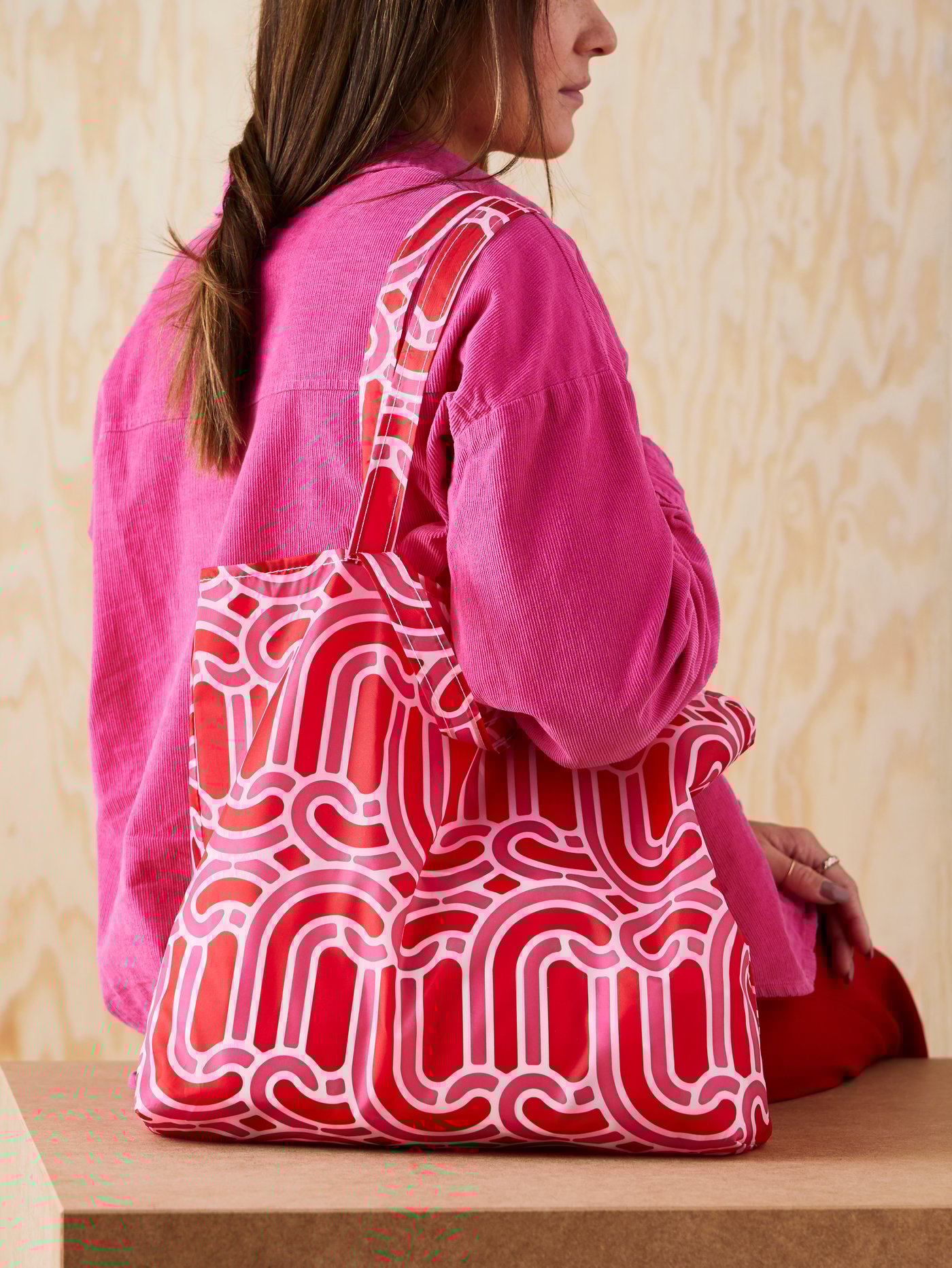 شخص يرتدي قطعة علوية وردية اللون يجلس على سطح خشبي مع كيس تسوق   SÖTRÖNN على كتفه الأيمن.