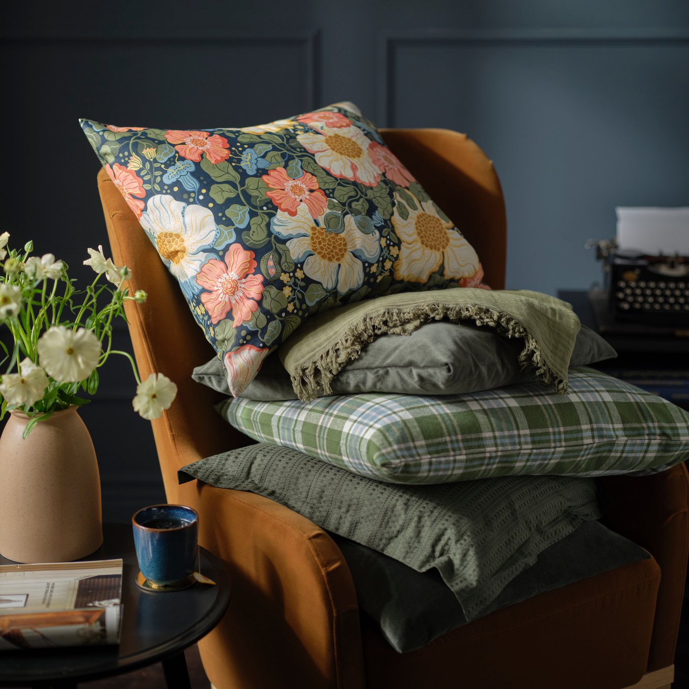 An orange armchair is filled with pillows in ARENBOK pillowcases along with green-checkered and green pillowcases.