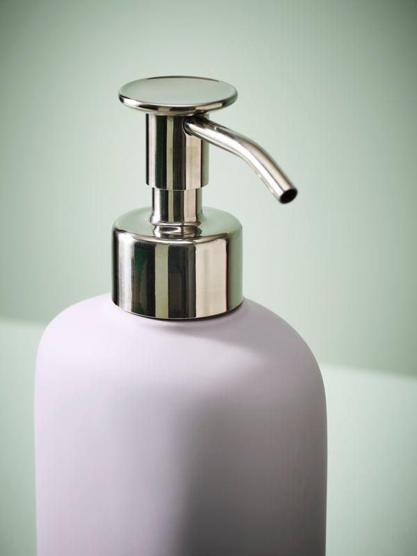 The stainless steel pump head of a lilac EKOLN soap dispenser against a light green backdrop.