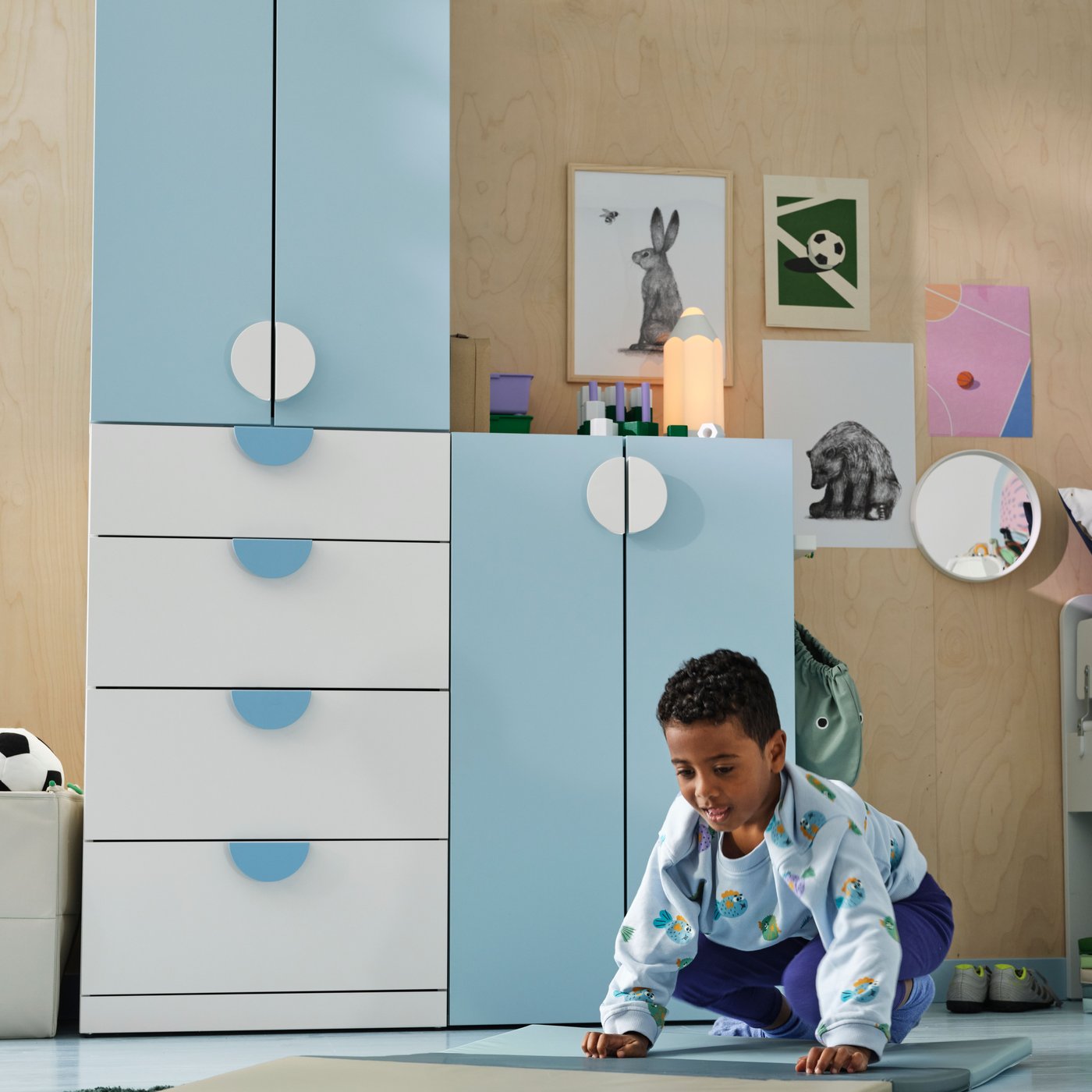 A child on a blue/green mat in a room with a light blue and white LASTARE storage combination, animal posters on the wall.