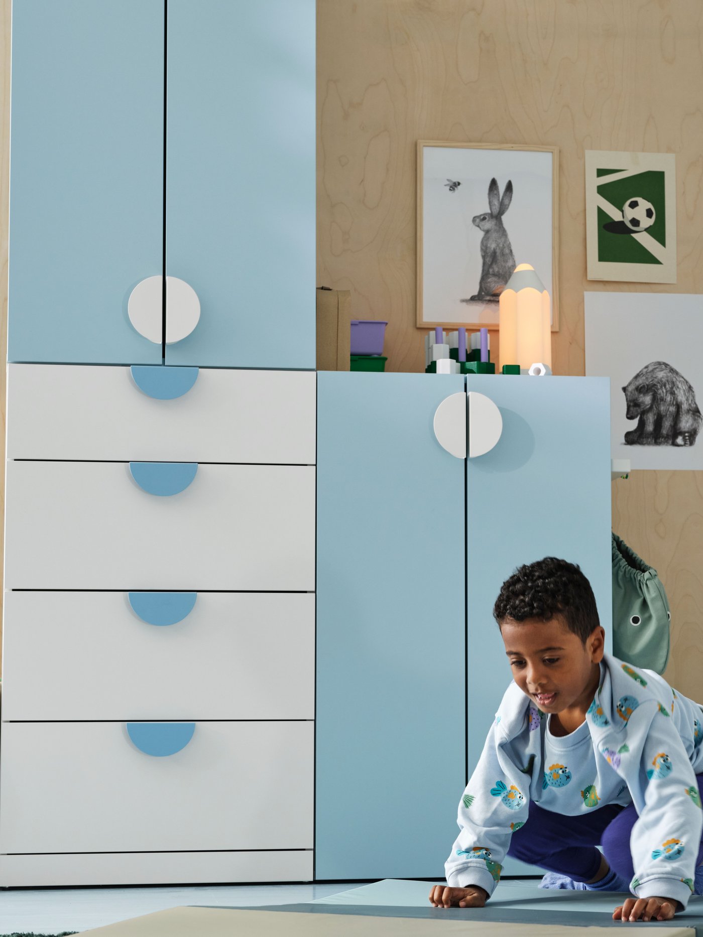 A child in a children's room with a light blue and white LASTARE storage combination, animal posters on the wall. 