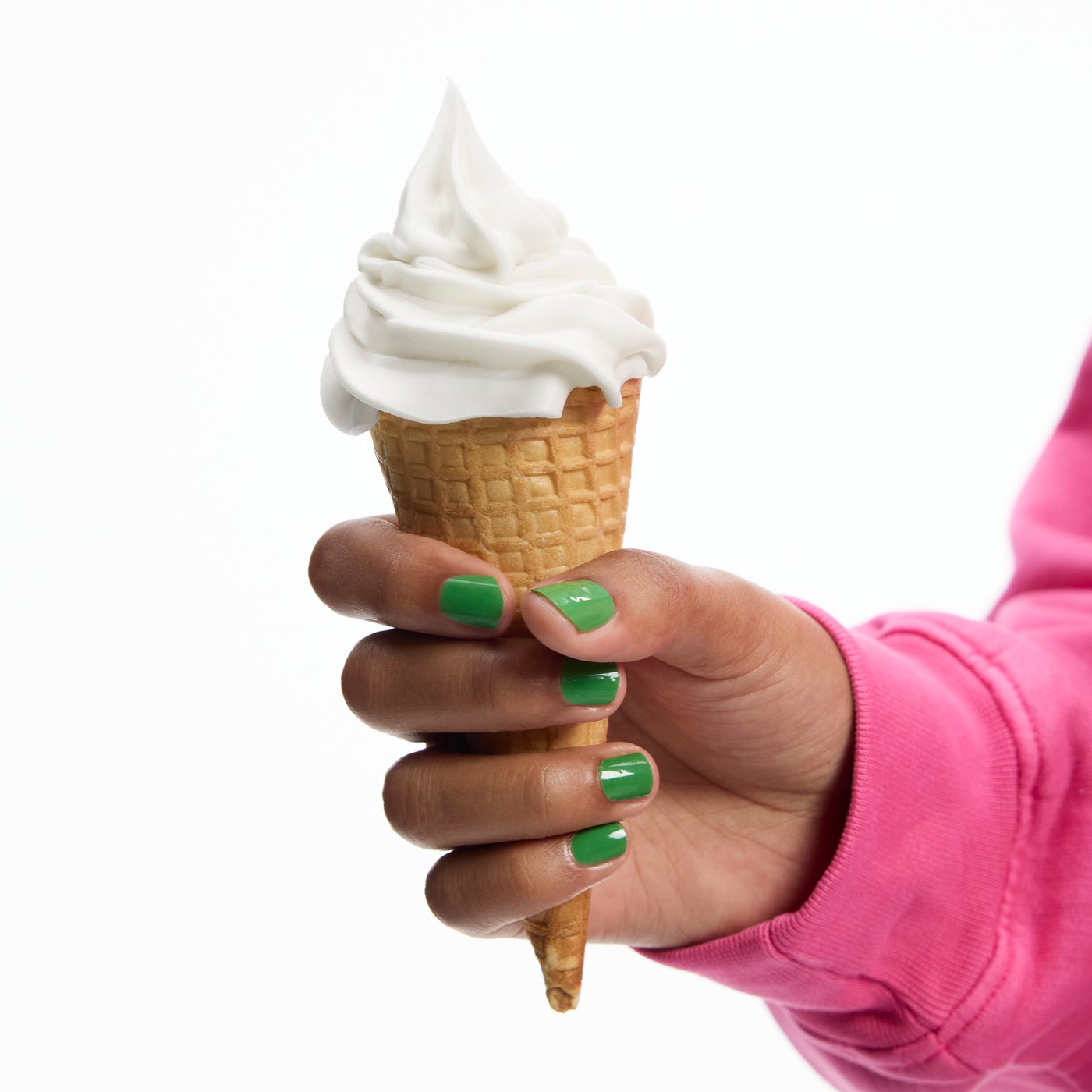 A hand with green nail polish is holding a creamy soft ice cream cone.