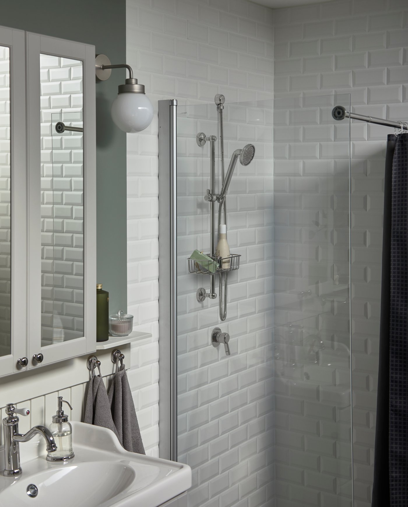 A mirror cabinet and wash-basin in white, a white-tiled shower and a head shower and a shower shelf that are chrome-plated.