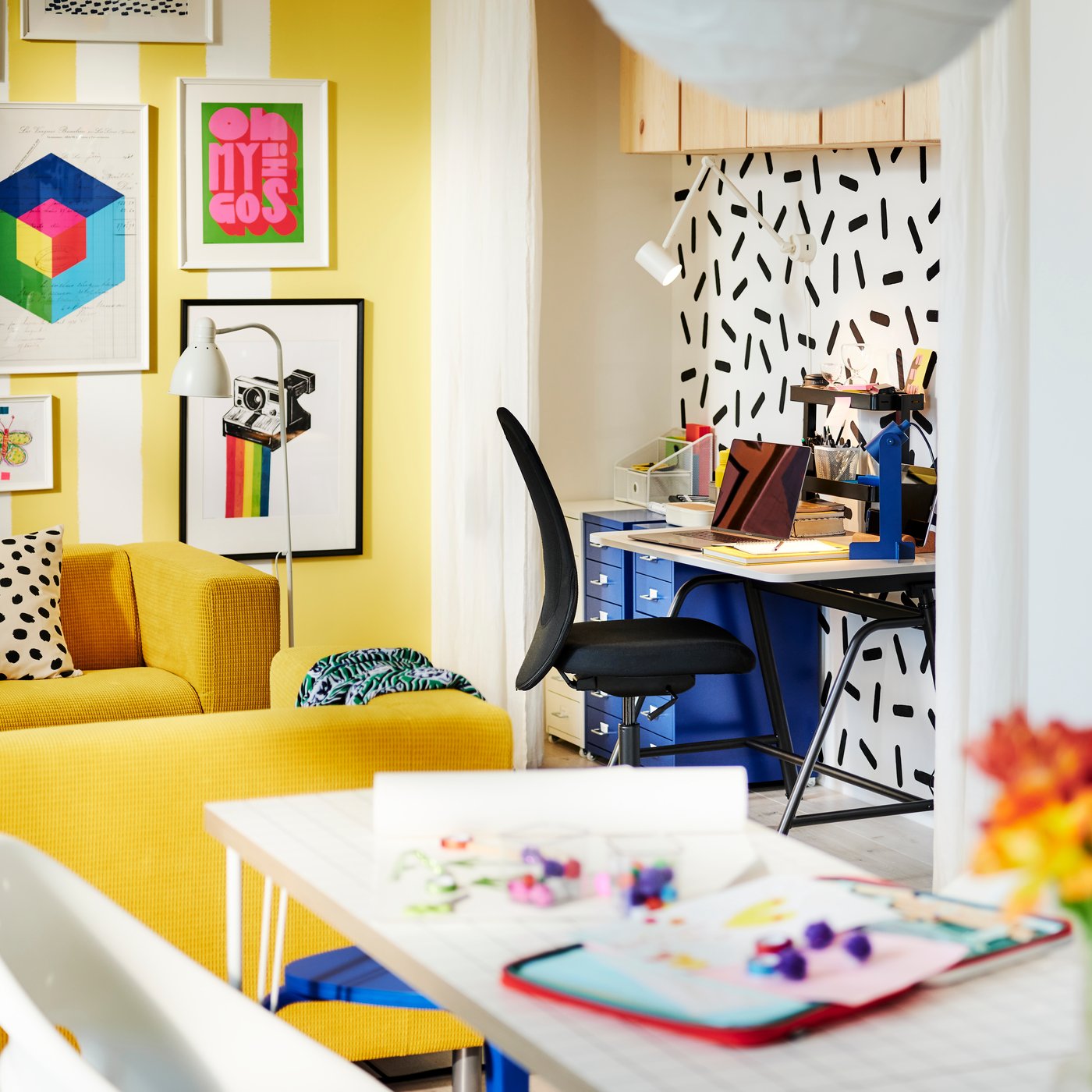 Ett ljust, färgglatt och rymligt rum. En arbetsplats med ett GLADHÖJDEN sitt-/ståskrivbord är placerad vid en grafiskt mönstrad vägg.