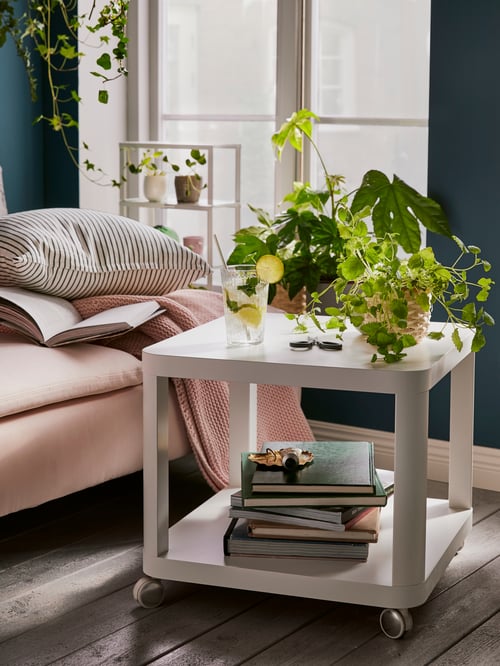 White TINGBY side table with castors in front of a pale pink SÖDERHAMN chaise longue. The table holds books and plants.