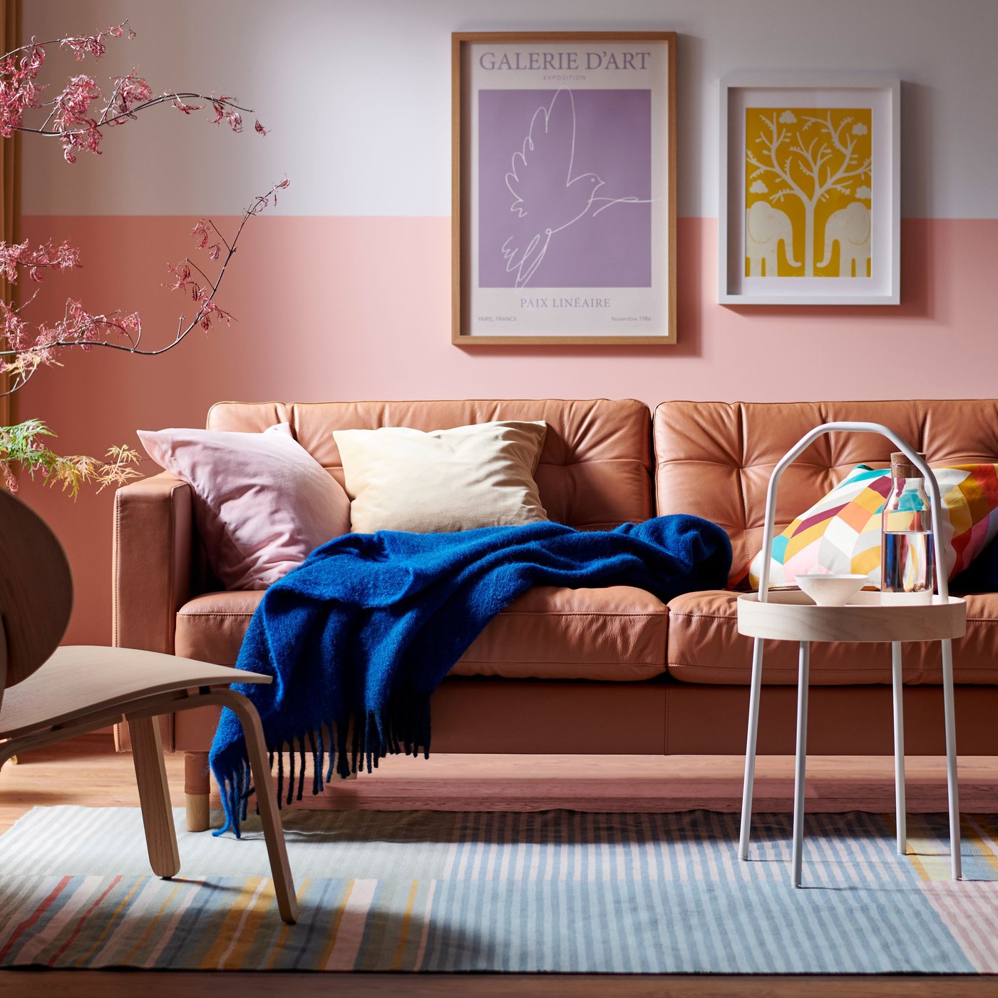 A LANDSKRONA sofa, with a blue KLIPPOXEL throw and extra cushions on it, and a BURVIK side table stand on a BUDDINGE rug.