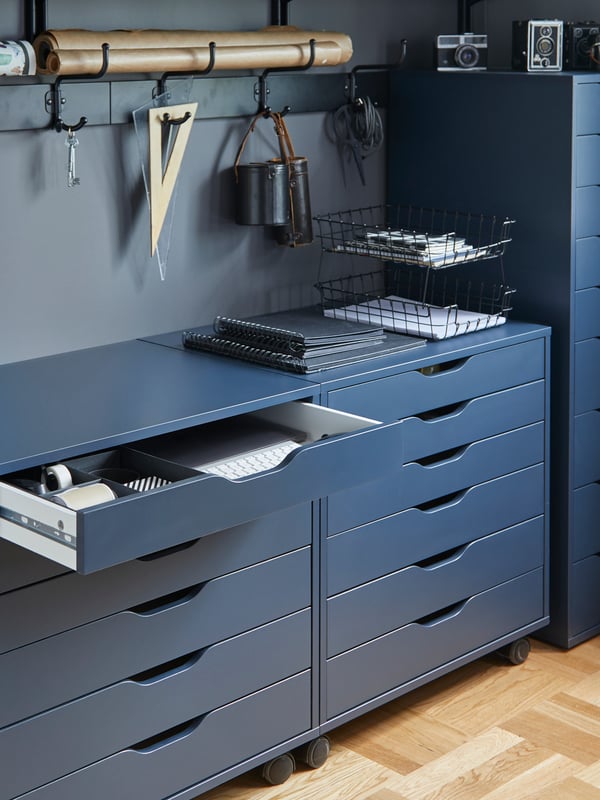 ALEX drawer units on castors, one draw is open and various office supplies hanging on the rear wall.