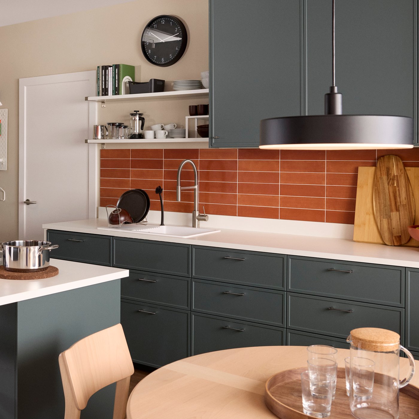 A bright kitchen has matte dark grey-green ASPUDDEN fronts and a kitchen island with a dining table in front.