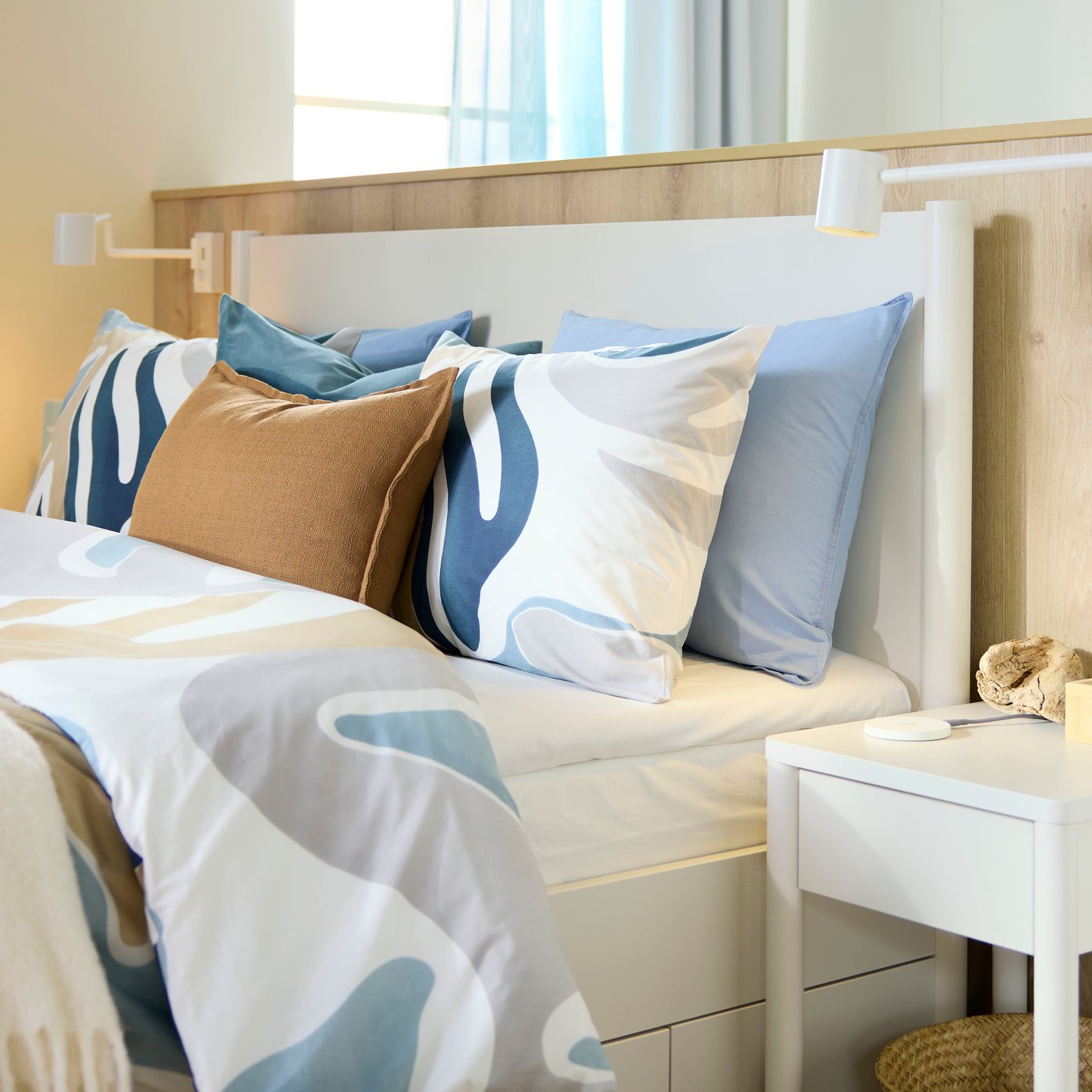 A bed has a leafy-patterned MYGGLASVINGE quilt cover and pillowcases on it, against a low wall in a light-filled hotel room.