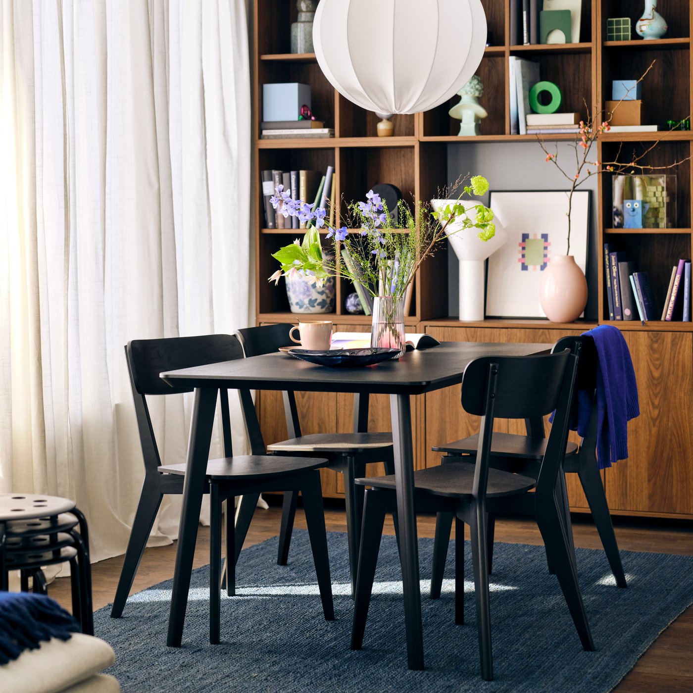 A dining room with a black LISABO table with a plate, a cup and a vase of flowers, surrounded by black LISABO chairs.