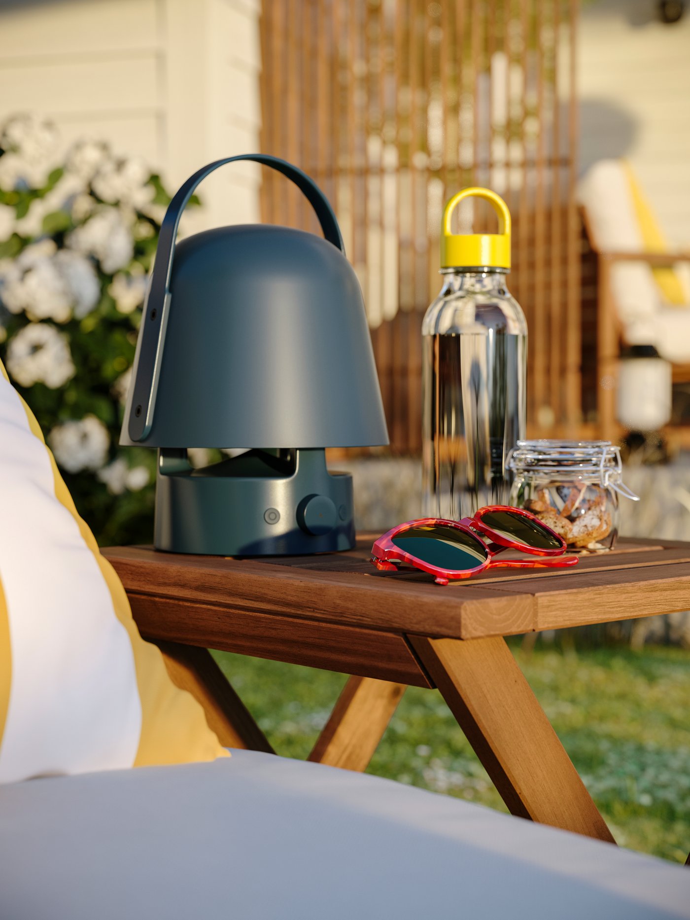 A close-up of a NÄMMARÖ outdoor stool with a VAPPEBY Bluetooth speaker lamp, sunglasses, a bottle and a jar on it.