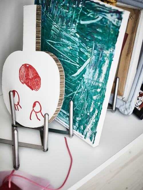 A close-up inside a kitchen cupboard, where a stainless steel VARIERA pot lid organiser holds an array of art projects.