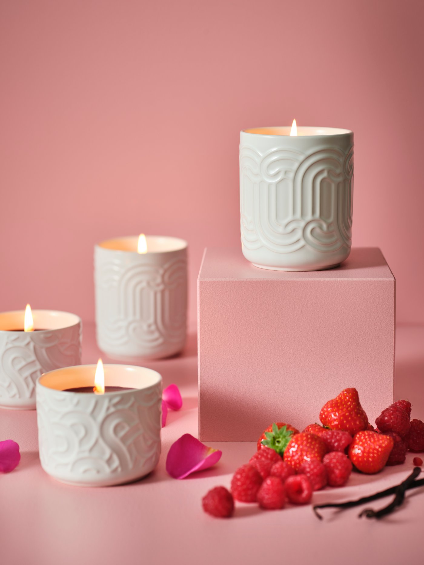 Four lit SÖTRÖNN scented candles in a pink space. One is on a pedestal. There are strawberries next to the pedestal.