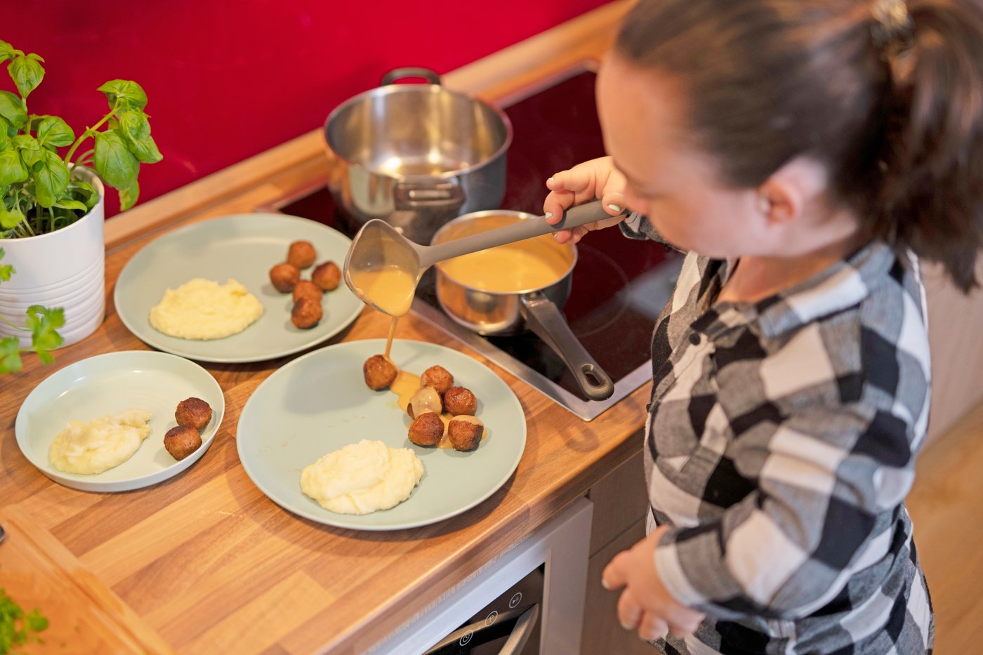 キッチンにいる女性がHUVUDROLL/フヴドロル プラントボールとALLEMANSRÄTTEN/アレマンスレッテン マッシュポテトを盛り付けたプレートにALLEMANSRÄTTEN/アレマンスレッテン クリームソースをかけている。 