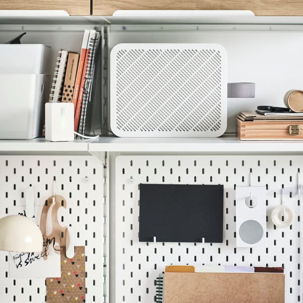 Two white SKÅDIS pegboards with accessories attached under a shelf with books and an UPPÅTVIND air purifier.