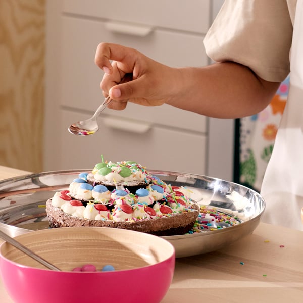 A three layer KAFFEREP chocolate cake decorated with cream, gets the final topping of green, blue and red candy.