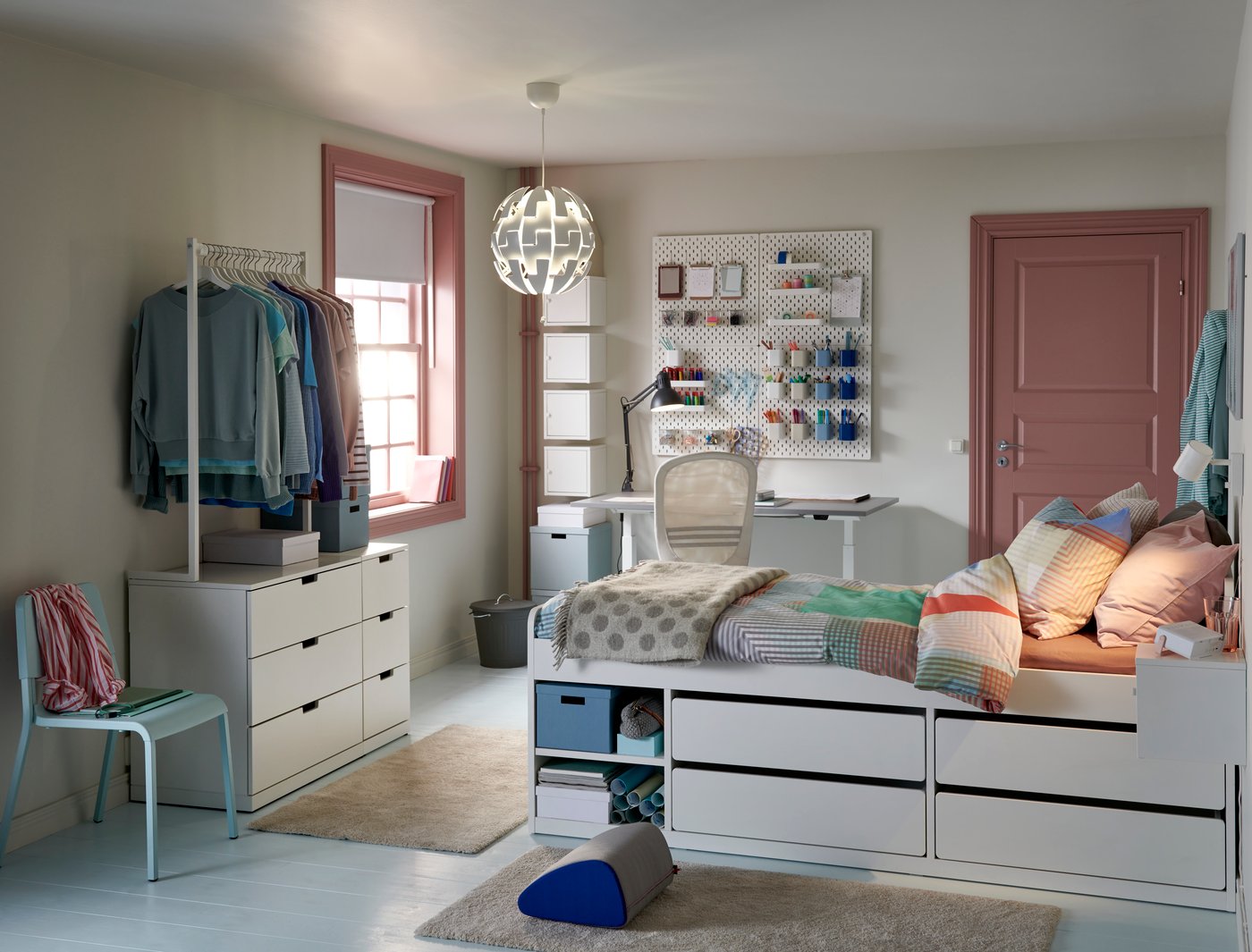 Habitación de estudiantes en colores pastel con una cama con un espacio de almacenaje integrado, un escritorio y un armario para colgar ropa cerca.