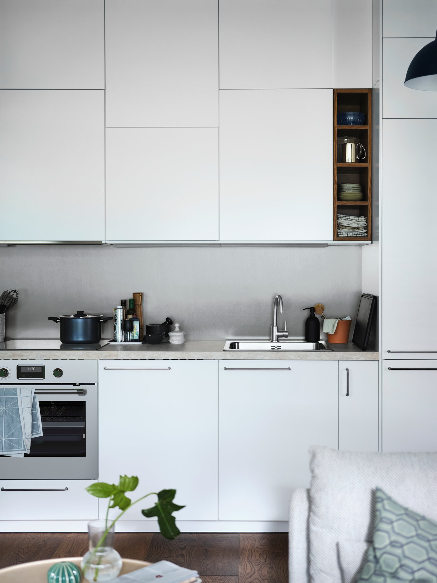 Cocina con un armario bajo blanco para fregadero, un grifo, armarios bajos, armarios de pared, una solución de almacenaje abierta marrón y un horno.