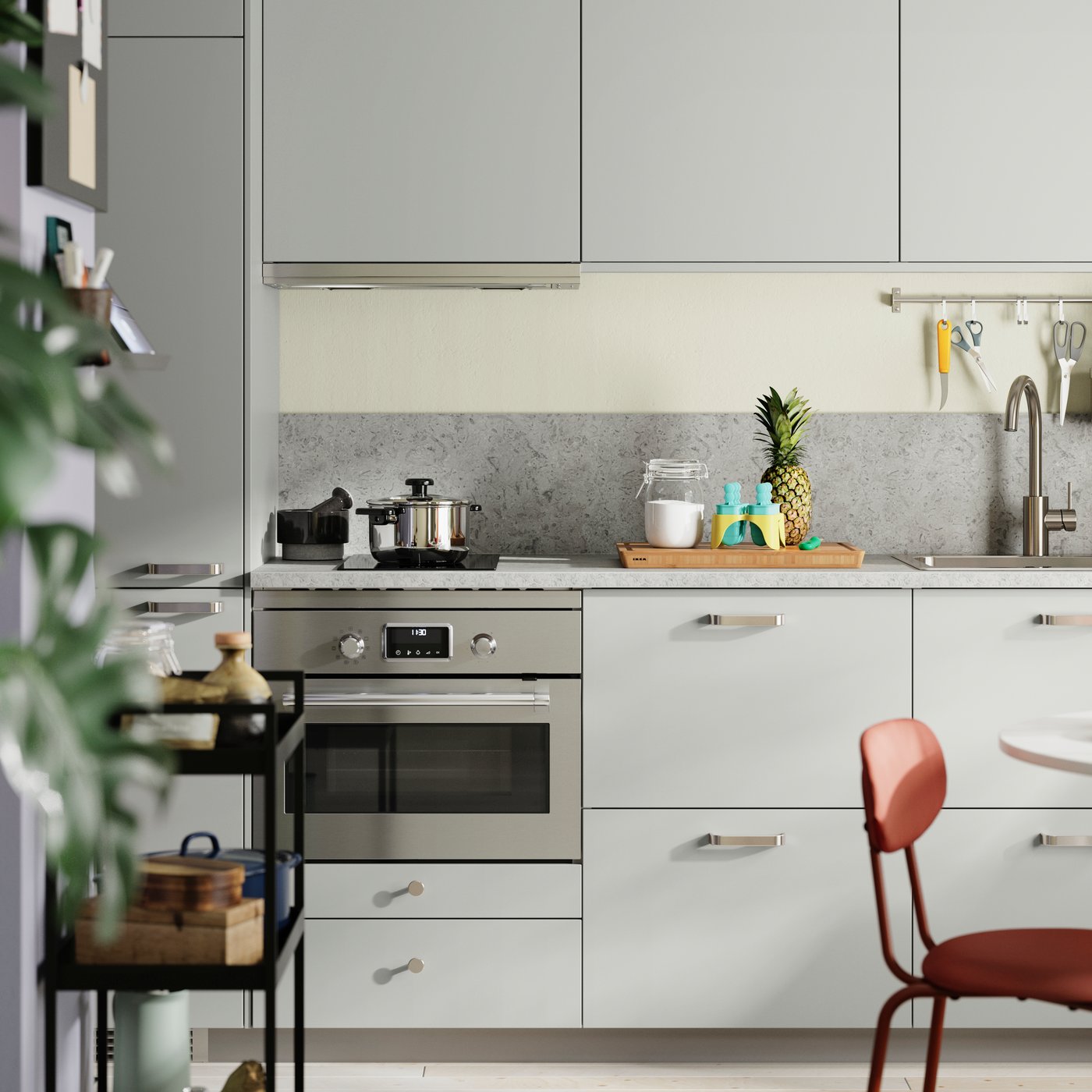 A small and straight kitchen with light grey HAVSTORP fronts has a colourful dining area and green plants in the foreground.