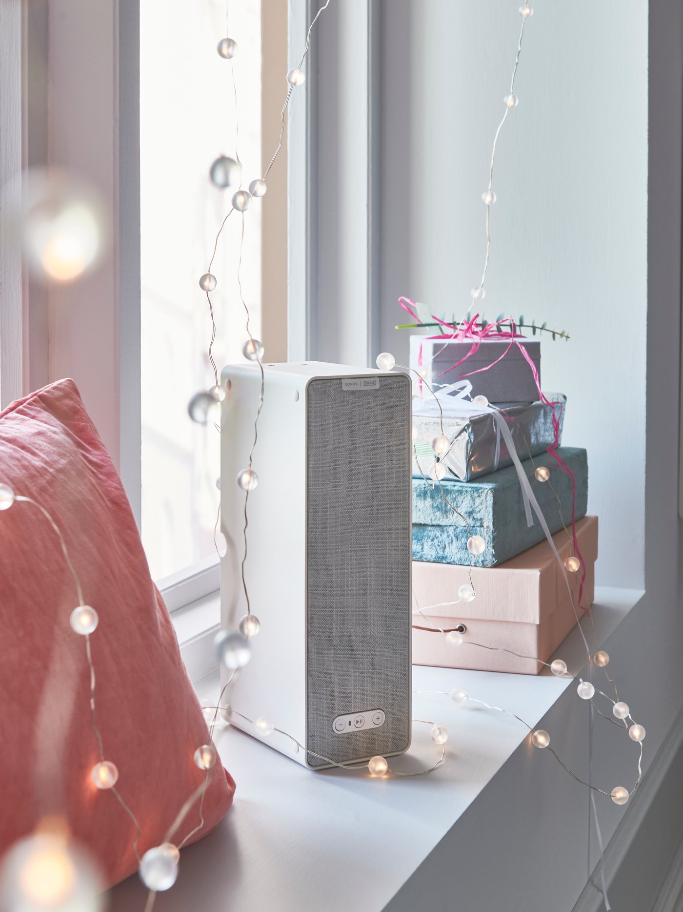 The SYMFONIK white WiFi bookshelf speaker by the windowsil can be controlled with IKEA Home Smart App.