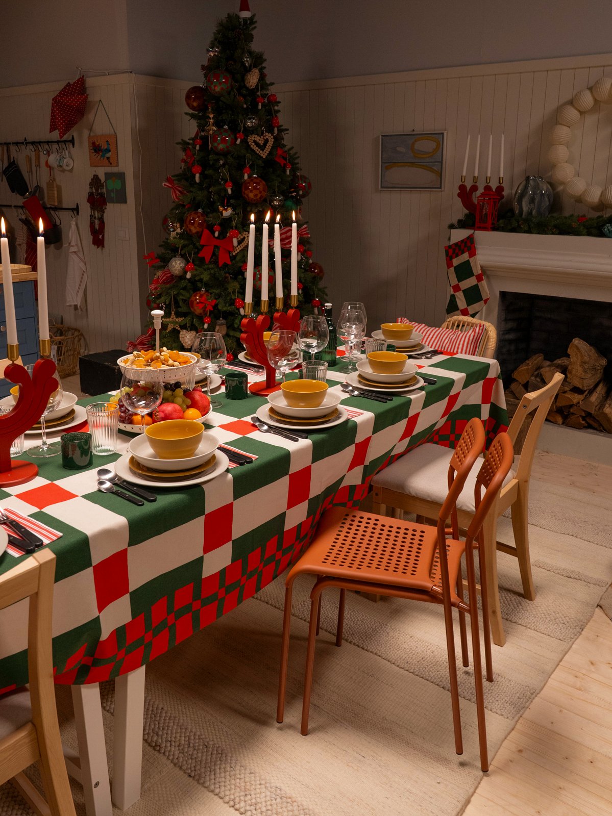 Una tavola imbandita per le feste di Natale, con una tovaglia a quadri verdi e rossi, ciotole gialle e candele accese. Sullo sfondo, un albero di Natale e un camino creano un'atmosfera calda e accogliente.