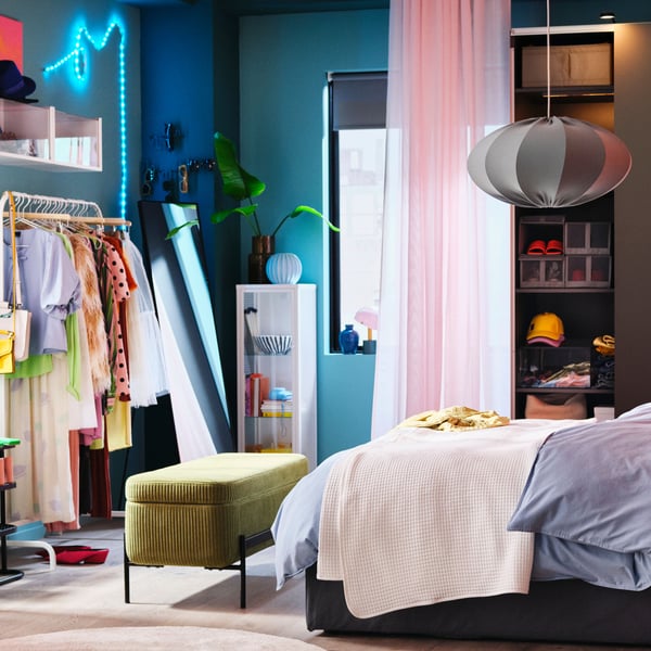 Ett färgstarkt sovrum med en BLÅFJÄLLET ottoman divansäng framför en mörkgrå HASVIK garderob och en rosa gardin.