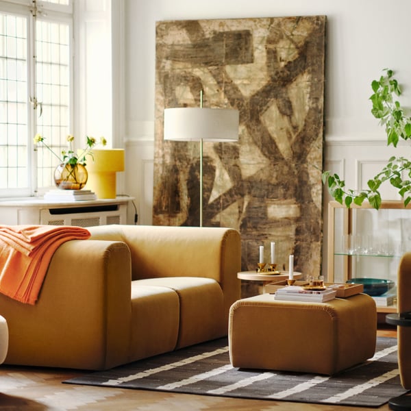 Un soggiorno luminoso con due divani a 2 posti STOCKHOLM 2025 beige posizionati uno di fronte all'altro, più un pouf e un tappeto in mezzo.