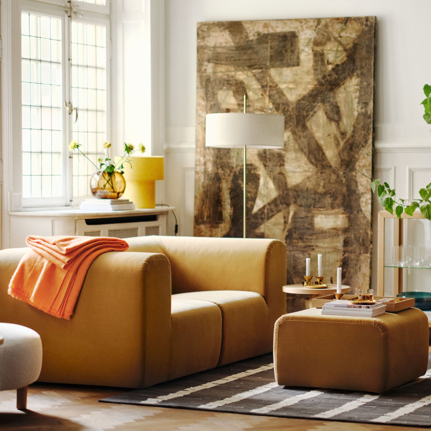 A bright living room with two beige STOCKHOLM 2025 2-seat sofas facing each other, with a pouffe on a rug between them.