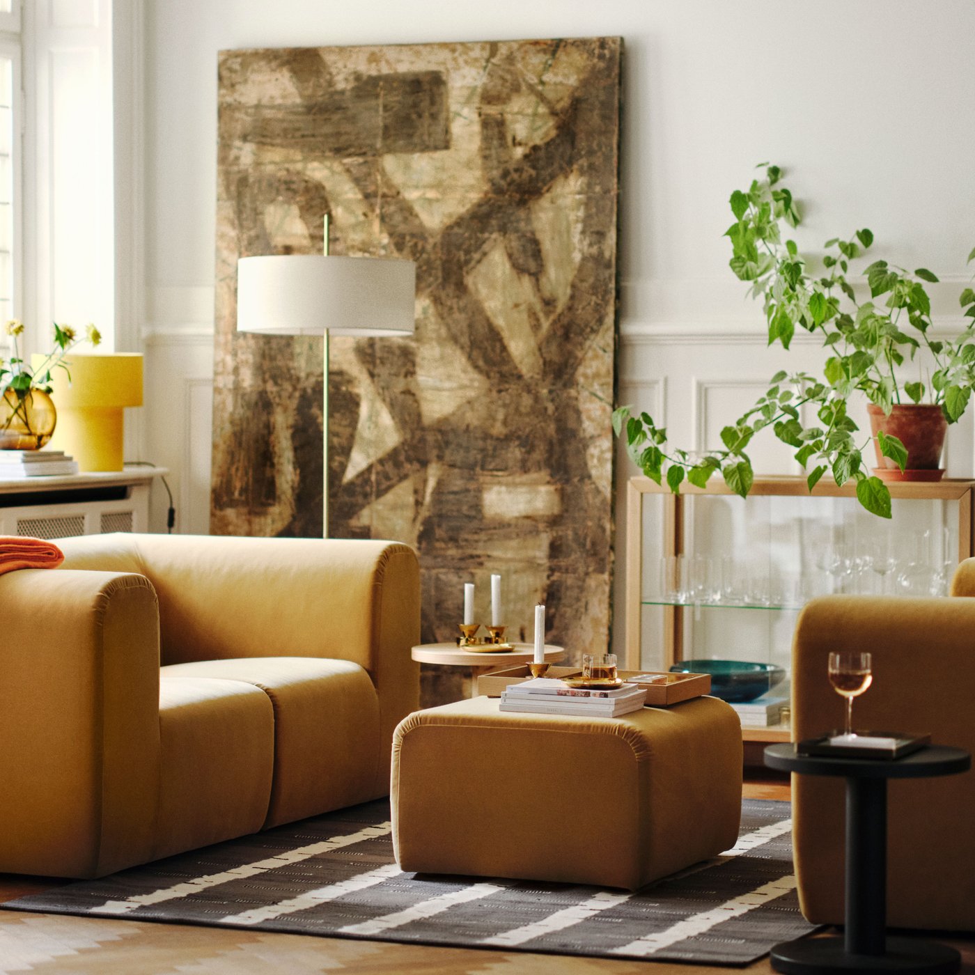 Sala luminosa com dois sofás de 2 lugares STOCKHOLM 2025 em bege de frente um para o outro, com pufe sobre tapete entre eles.