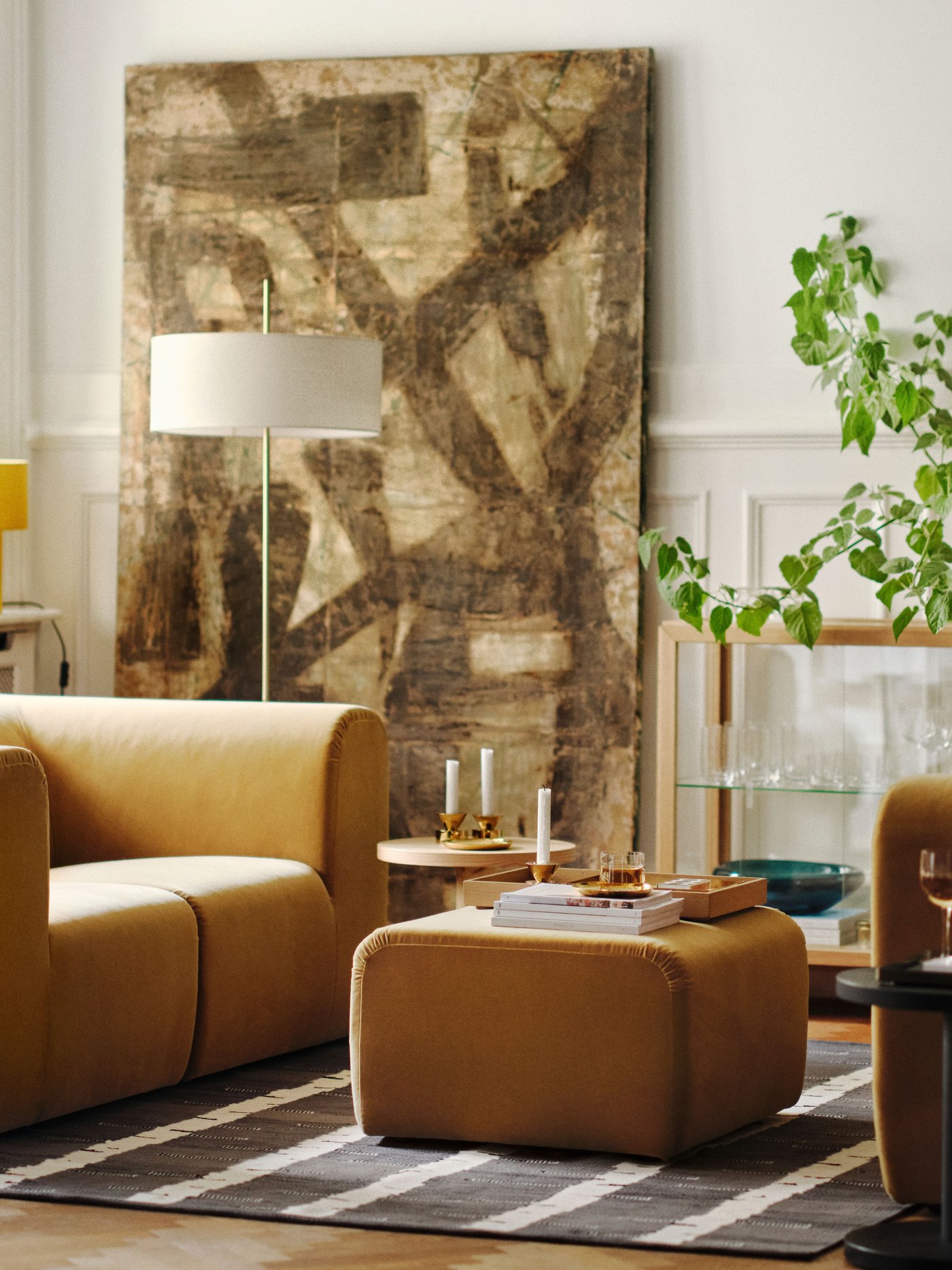Helles Wohnzimmer mit zwei beigen STOCKHOLM 2025 2er-Sofas, die sich gegenüberstehen, und einem Pouf auf einem Teppich dazwischen.