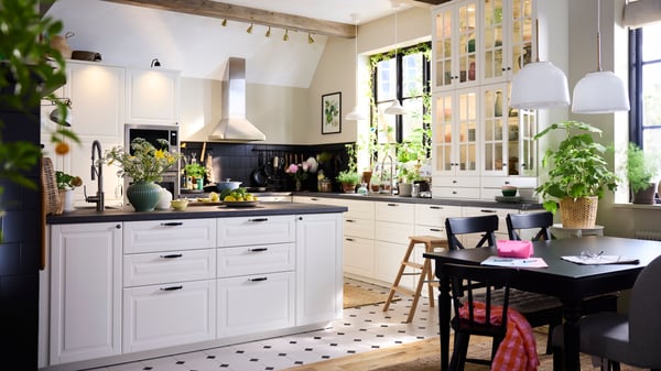 Bright farmhouse-style kitchen with white cabinets, black accents, plants and dining area.