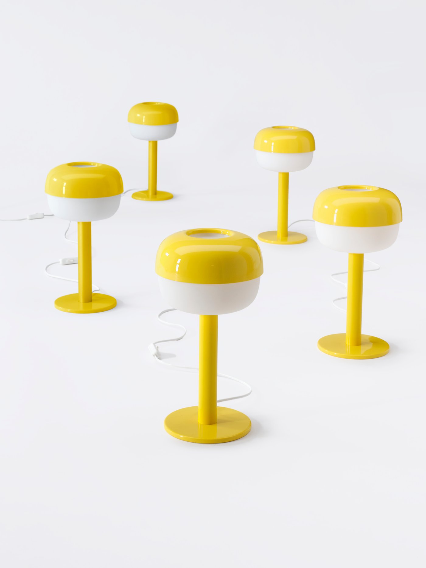 Cinque lampade IKEA gialle allineate su un pavimento bianco.