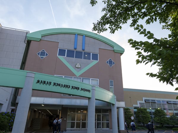 緑とベージュを基調とした建物の外観。日本語の看板がある、教育機関の入口。