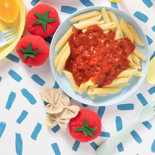 Un piatto di pasta al sugo con accanto dei giocattoli di peluche con forma di alimenti