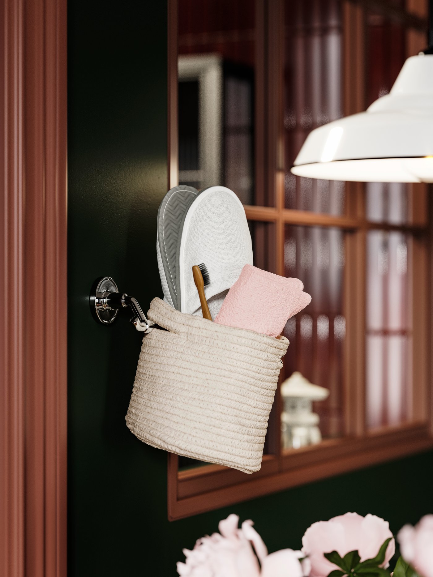 En TJABBIG-korg hänger på väggen med tofflor, en rosa handduk och en borste, mot en mörkgrön och rödbrun bakgrund.