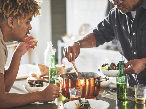 Zwei Personen verteilen Essen aus einem Topf auf Teller.