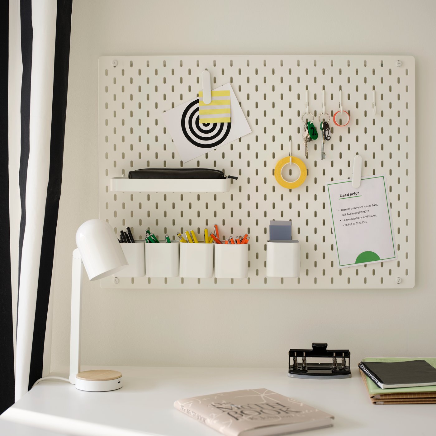 Een wit SKÅDIS ophangbordcombinatie aan een wand boven een bureau.