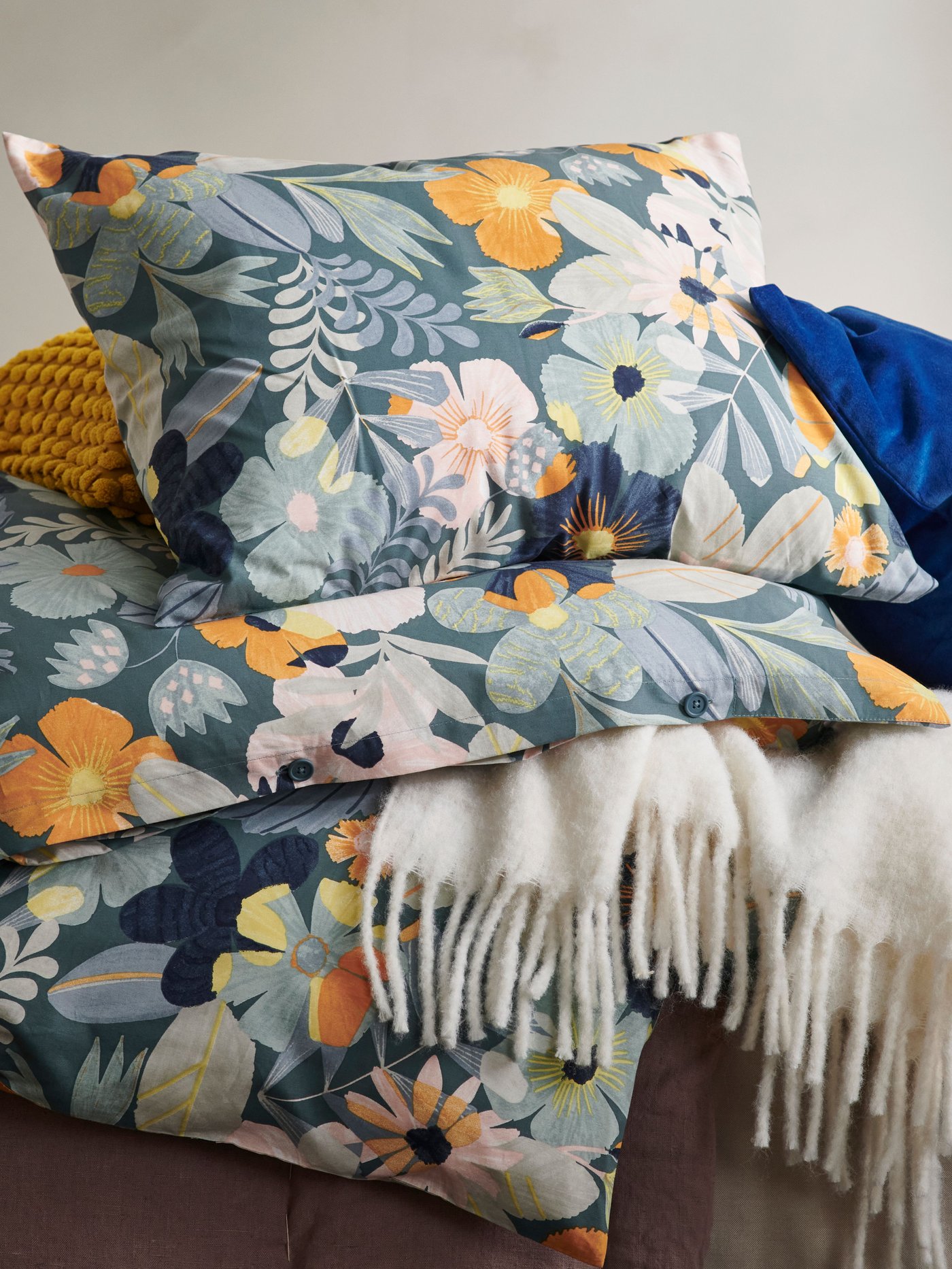 A floral bedding with a tan blanket next to it.