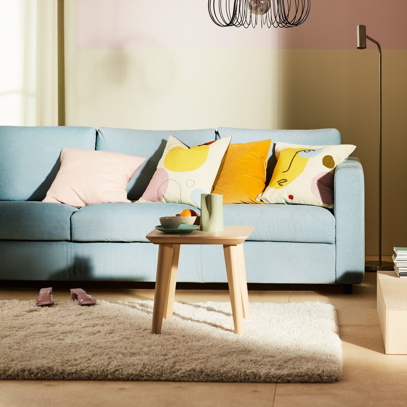 A light blue VIMLE 3-seat sofa with colourful cushions on it and a high pile VOLLERSLEV rug in front of it.