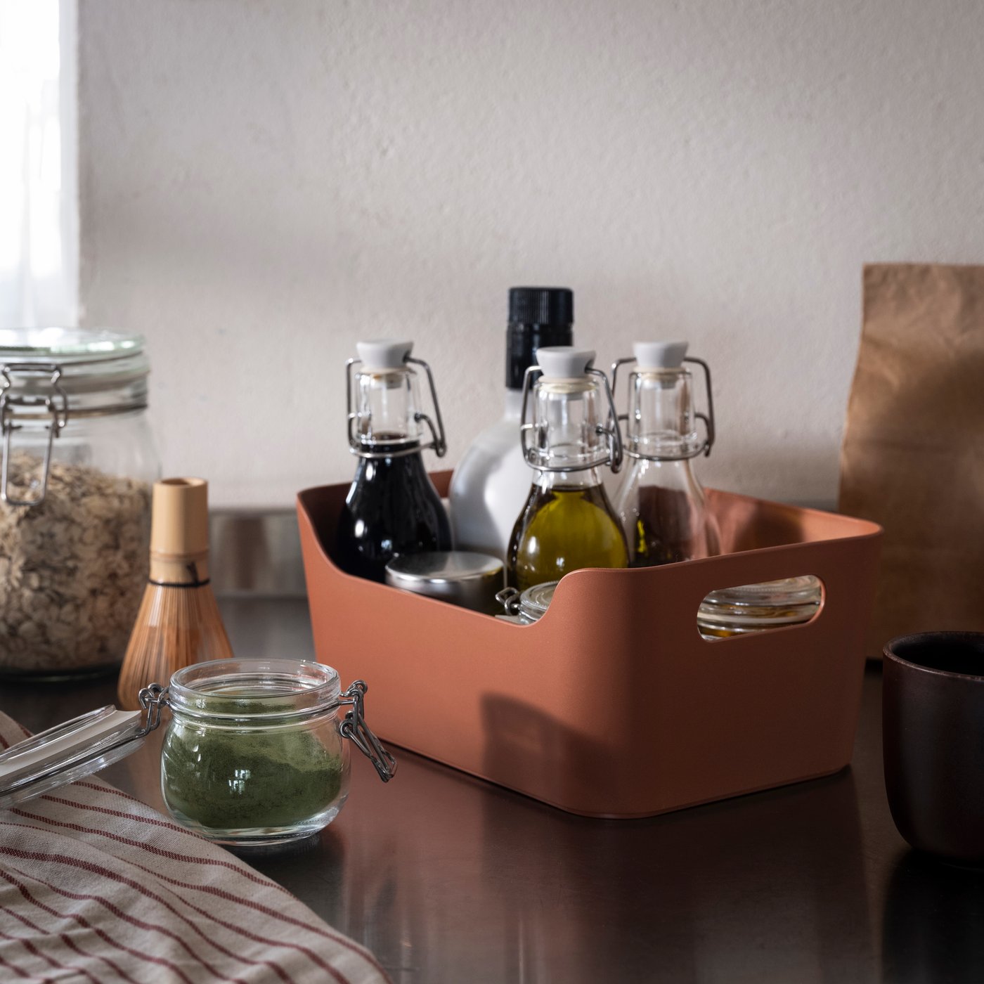 Uppdatera box in red-brown colour, holding kitchen spices and oil bottles, on the kitchen counter.