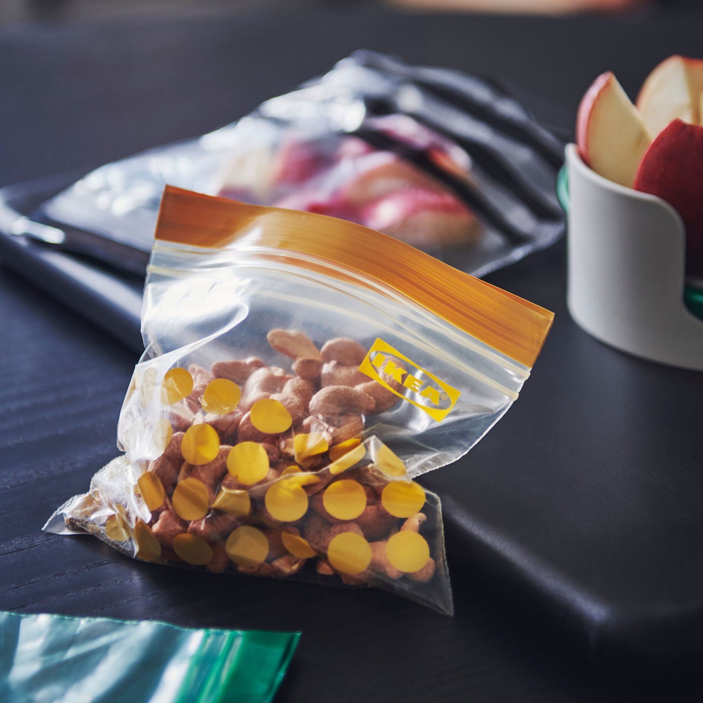 Cashew nuts inside an ISTAD resealable bag with a yellow pattern and apple slices in a bag with a black pattern.