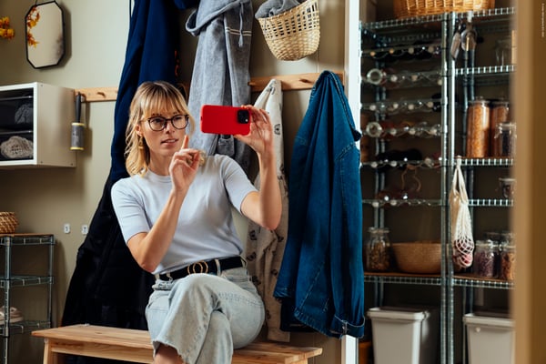 Close-up of a persons hands holding a tilted smartphone displaying the KREATIV function in the IKEA app, visualising a furnished livingroom.
