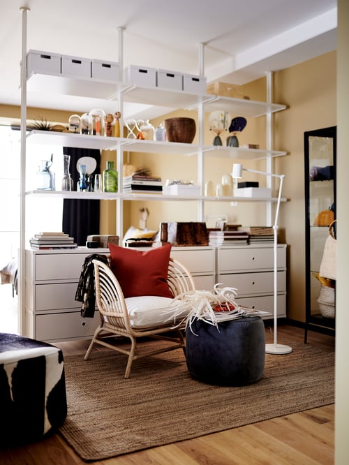 Living room with open storage combination, armchair, reading lamp, pouffe, storage boxes with lids, rug, cushion covers.