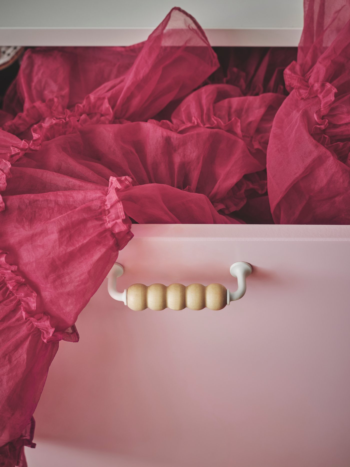 Detalle de un asa con cuentas sujeta a una caja rectangular rosa que contiene una tela rosa oscuro.