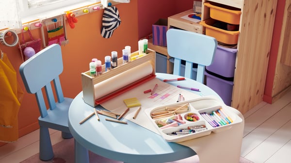 Two children’s chairs and a children’s table from the MAMMUT series in light blue. Art materials are laid out on the table.