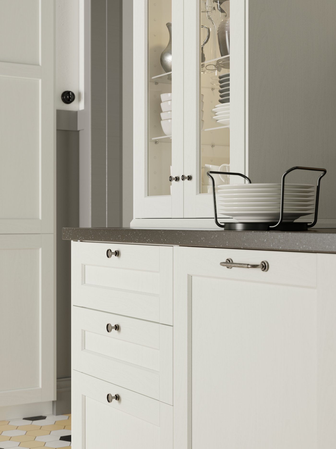 A cabinet with white ENKÖPING glass doors on a countertop, holding bowls, plates and jugs, with a plate holder on the side.